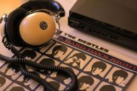 Fugue Beatles Retro Reverie – A 1970s Hi-Fi Headphone & Beatles Vinyl Still Life A vintage 1970s hi-fi headphone rests gracefully on a turntable, its padded ear cups and coiled cord whispering of analog warmth. Beside it, a weathered Beatles LP leans against the player. The golden morning light catches the dust motes hovering above the scene, as if time itself paused to listen. A love letter to tactile music, crackling imperfections, and the ritual of dropping the needle. 