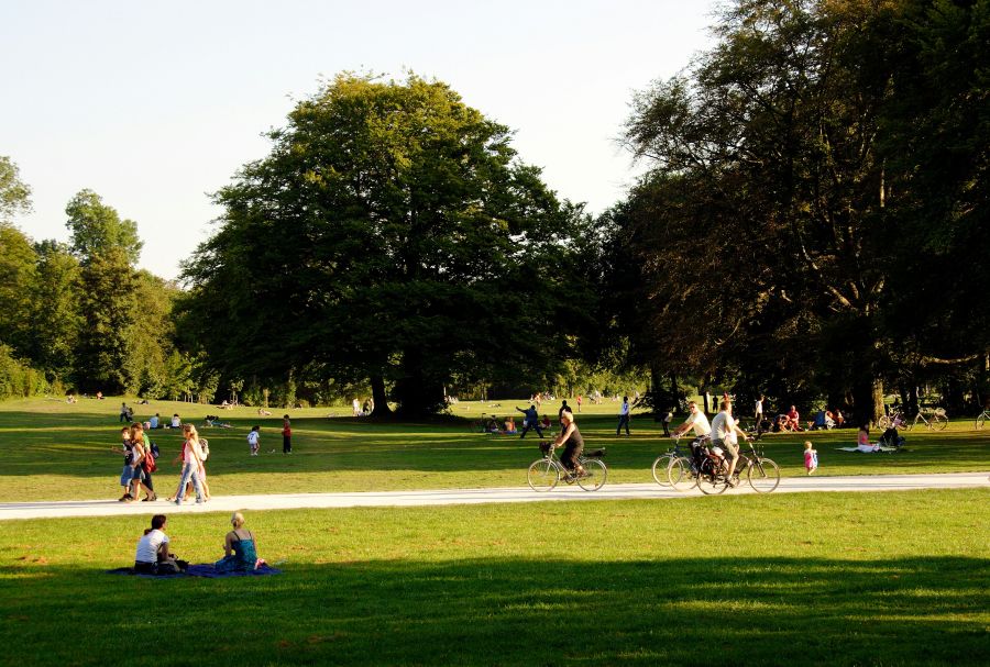 park Many people enjoy the afternoon sun on the meadows of the English Garden, sitting and lying; others walk or ride a bicycle. 