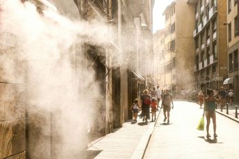 heat wave Summer street scene in Firenze, Italy, during a heatwave. People walking under the strong Tuscan sunlight with refreshing water mist in the urban atmosphere.