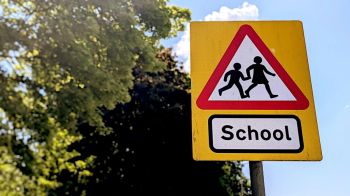 Child safety Classic British yellow school warning sign featuring children crossing, set against trees and a bright blue sky 