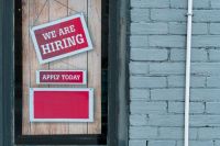 job recruitment We Are Hiring Sign in Window of Brick Building - A red and white sign in a window of a brick building reads We Are Hiring with a smaller sign that says Apply Today. 