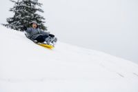 sled A boy laughs while sledding down a hill. 