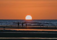 Beach soleil Sunset on a beach in summer, with reflections on the water. A family stands in a line in front of it. 