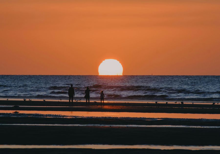 Beach soleil Sunset on a beach in summer, with reflections on the water. A family stands in a line in front of it.