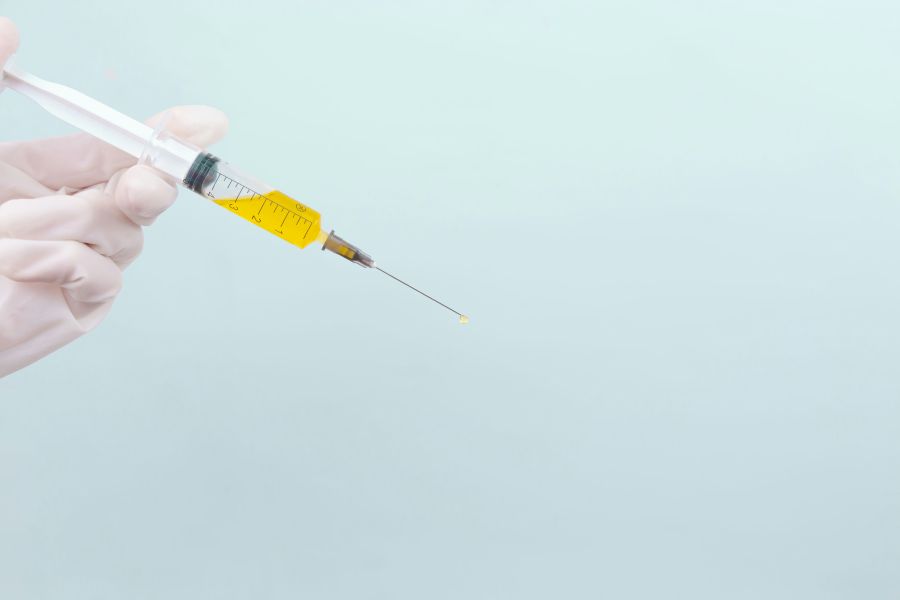 Narcotics drug The doctor's hand in a white medical glove holds a syringe with a yellow medicine on a blue background. The medicine. Place for an inscription. Vaccine. Covid 19. Coronavirus. vaccine,wellness,injection