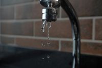 Water waste faucet drops water on brick background 