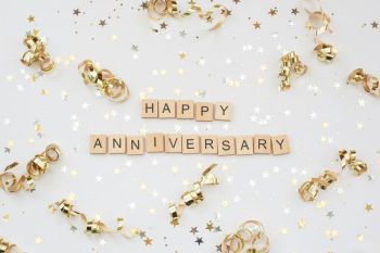 celebration anniversary The words 'HAPPY ANNIVERSARY' in wooden letter tiles, surrounded by gold and silver coloured stars and gold curls, all set against a white background.