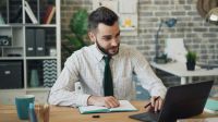 Accord occupation Bearded guy using laptop typing writing in notebook sitting at table in office person,man,male