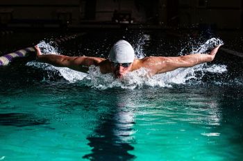 Swimming Running Male swimmer racing the butterfly stroke in athletic pool.
