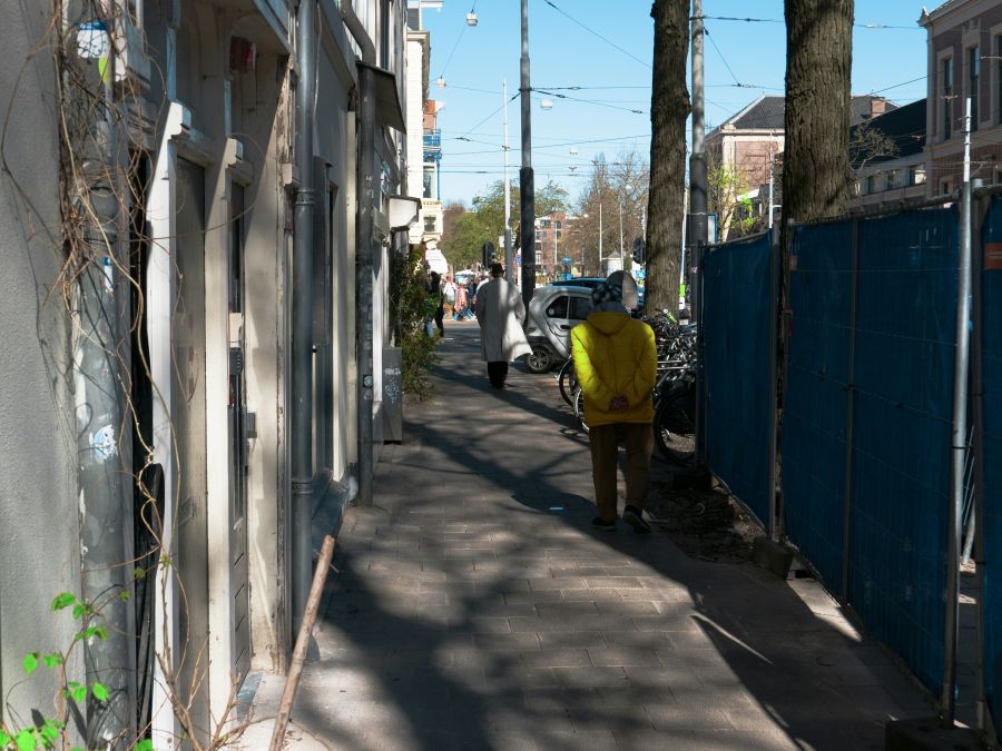 Local producers Photo of a narrow sidewalk with people walking in the street because there are construction works, so a building fence is necessary here. This is the Plantage district in Amsterdam city. I like in this image the deep view of the street, and the play of tree shadows on the brick pavement. This gives a lot of shades in light and in shadows, The house facades at the left are very sensitive for the light. Urban street photography of Amsterdam - Free people photo of The Netherlands, Fons Heijnsbroek. shades,brick texture,street people