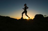 Trail running A woman runs up a trail during sunset.  