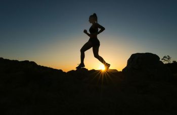 Trail running A woman runs up a trail during sunset.