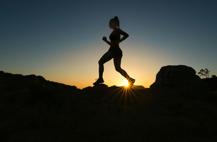 Trail running A woman runs up a trail during sunset.  