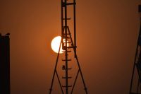 Sciences Po The image shows a Sun rise behind a latticework telecommunications tower. The sun is a deep orange color, and its light is reflected off the metal struts of the tower. The sky is a gradient of orange, pink, and purple. There are a few wispy clouds in the sky. science,mba,law