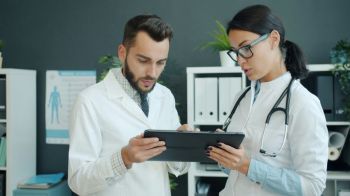 health innovation Medics in white gowns young man and woman are using tablet at work talking using gadget in office. Modern devices, people and technology concept.