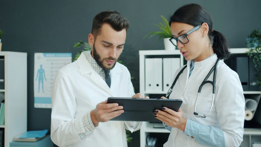 health innovation Medics in white gowns young man and woman are using tablet at work talking using gadget in office. Modern devices, people and technology concept. 