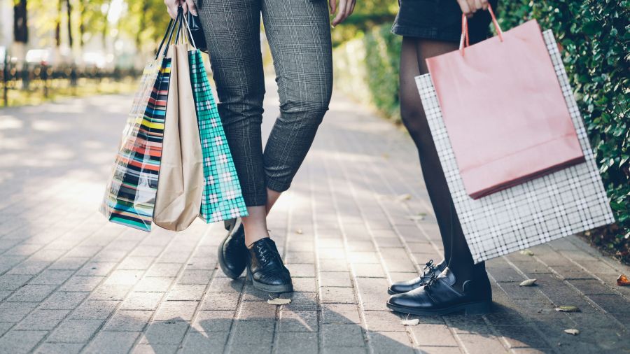Shopping street Low angle shot of female legs standing on sidewalk holding colorful shopping bags after happy busy day in shops and malls. People, consumerism and leisure concept. 