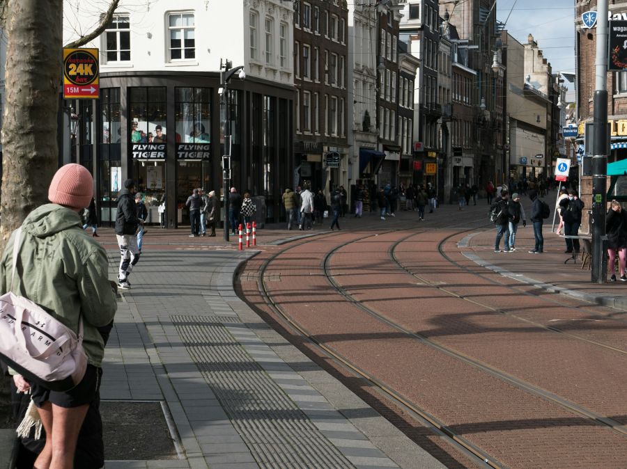 Weather Sunny Photo of Amsterdam city, free download: man is waiting for the tram along the tram track at sunny square Rembrandtplein. In the background people walking in Reguliersbreestraat, Winter 2022. Photo, Fons Heijnsbroek - street photography of The Netherlands in high resolution image of Amsterdam. // Foto van Amsterdam Rembrandtplein, gratis downloaden: een man wacht bij de tram en mensen lopen over het zonnige Rembrandtplein en in de schaduwen in de Reguliersbreestraat, winter 2022. Foto, Fons Heijn amsterdam,rembrandtplein,netherlands