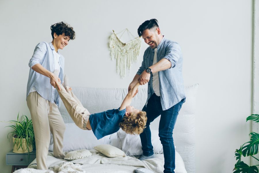 family drama Mother father swinging child holding hands and feet then putting on bed at home 