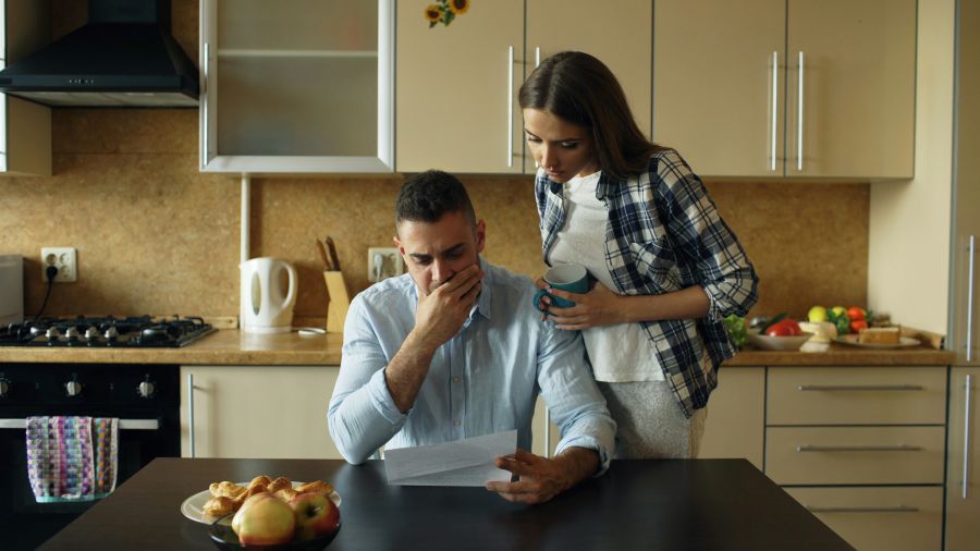 family budget Upset young man reading unpaid bills and hugged by his wife supporting him early morning in the kitchen at home 