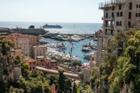 Mediterranean travel Port Hercule in Monaco glitters with rows of super-yachts and a visiting cruise liner, framed by Monaco’s cliff-side apartments. 