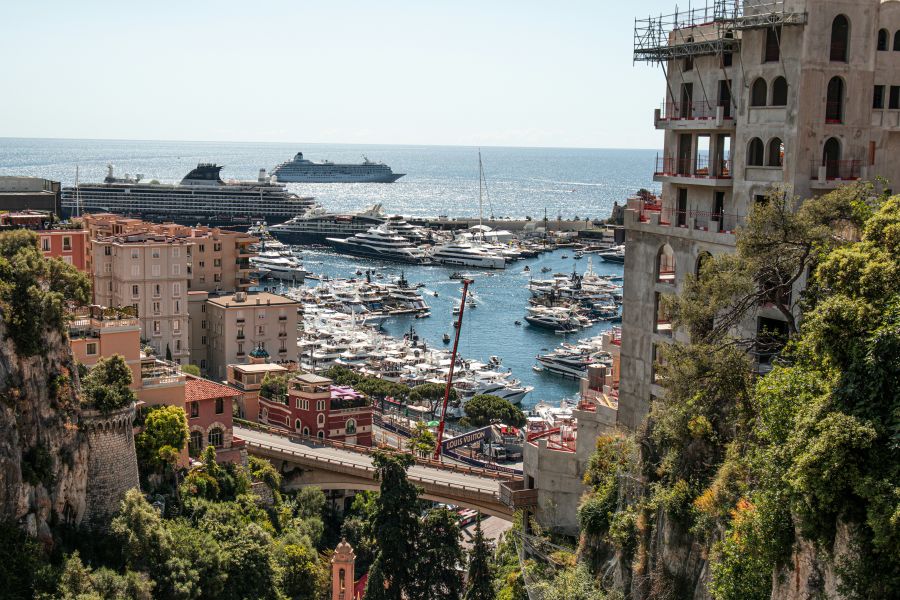 Mediterranean travel Port Hercule in Monaco glitters with rows of super-yachts and a visiting cruise liner, framed by Monaco’s cliff-side apartments. 