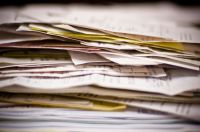 expenses report The image captures a dense, chaotic mountain of paperwork, specifically a thick stack of invoices, receipts, and documents that evoke the overwhelming feeling of tax season or complex financial record-keeping. 
