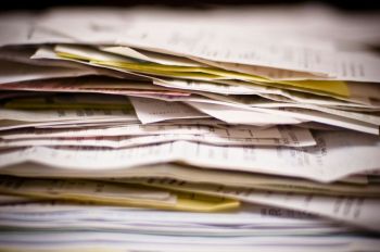 expenses report The image captures a dense, chaotic mountain of paperwork, specifically a thick stack of invoices, receipts, and documents that evoke the overwhelming feeling of tax season or complex financial record-keeping.