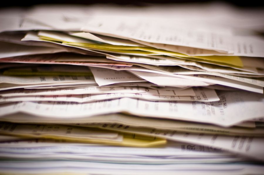 expenses report The image captures a dense, chaotic mountain of paperwork, specifically a thick stack of invoices, receipts, and documents that evoke the overwhelming feeling of tax season or complex financial record-keeping. 