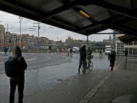 Cloudy rainy People are walking and standing under the cap of the station roof on a rany gray day in Amsterdam city. This is the station square with tram tracks and tile pavement. I like the grey shades and lights in this image. Typical Dutch weather. Street photography of people in old towns in The Netherlands, free photo by Fons Heijnsbroek, 2023 central station amsterdam,Urban,urban people