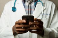 Doctor physician Doctor Holding Cell Phone. Cell phones and other kinds of mobile devices and communications technologies are of increasing importance in the delivery of health care. Photographer Daniel Sone   healthcare systems,physician practice,healthcare management