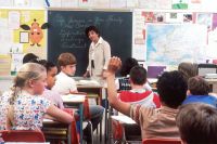 Teacher Children in a Classroom. In the back of a classroom, are children about 11 years old with a female teacher talking about the subject - If Someone in Your Family Has Cancer. Photographer Michael Anderson classroom,cancer,students