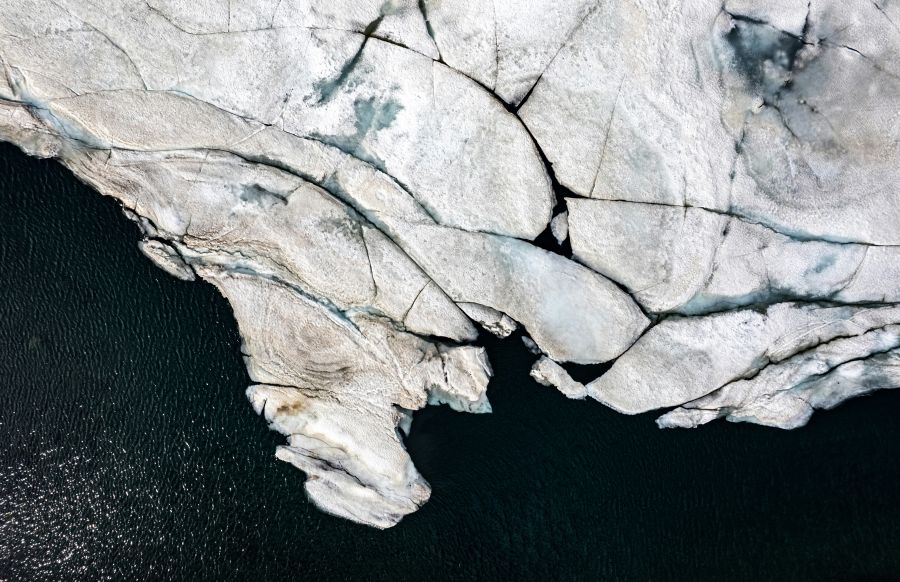 Geological expedition An aerial view captures the intricate patterns of a glacier's surface, where the interplay of ice and rock creates a natural mosaic. The texture of the glacier is palpable, with crevasses and melting snow revealing the rugged terrain beneath. The dark waters surrounding the ice hint at the deep cold of the environment. This image encapsulates the raw beauty and the impermanent nature of our planet's frozen landscapes. nature,grey,iceland