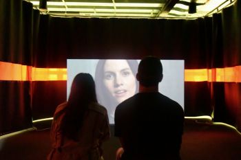 cult leader Two people mesmerized by a woman on a screen