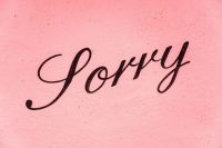 apology A sign saying sorry on a pink background. 