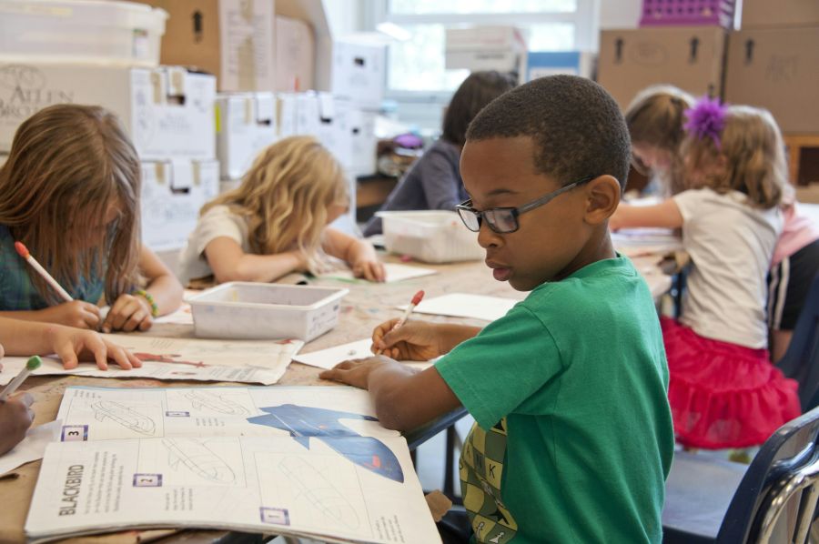 school Captured in a metropolitan Atlanta, Georgia primary school, seated amongst his classmates, this photograph depicts a young African-American schoolboy who was in the process of drawing with a pencil on a piece of white paper. Note that the student was focused on a drawing book that referenced fantasy flying planes, while intent on creating his artwork, seemingly oblivious to all the classroom goings-on that surrounded him. It is important to know that objects, including pencils, crayons, paper, e