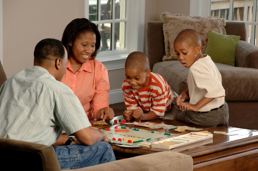 Handicap siblings Family Playing Board Game. An African-American family (adult male and female and two male children) sit around a coffee table playing a board game.  Photographer Bill Branson  siblings,family,cancer