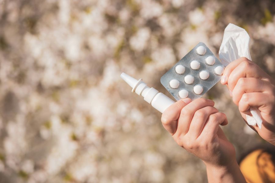 cold medication Allergy concept, young woman with pills or drugs and nose or nasal spray against the strong allergy in hand in front of blooming a tree during spring season, healthcare 