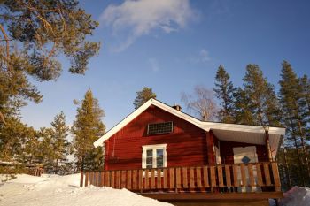 Swedish chalet A charming, rustic red cabin nestled amidst snow-laden Norwegian pines. Sunlight glints off a lone solar panel, hinting at a life lived off the grid in winter's embrace.