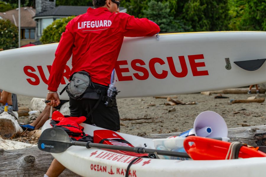 beach rescue 2026-07-10 Vancouver beach lifeguard red jacket carrying surf rescue surfboard. 