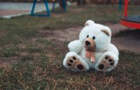 Missing child Cute adorable lost abandoned soft plush stuffed children toy teddy bear sitting on ground street road. In park outdoor. Lost lonely toy outside grey,sitting;,teddy