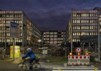 Cycling safety Twilight scene of an urban construction site with a cyclist in motion blur passing by, SAP building in the background, demolition debris, and safety signage prominently displayed. walldorf,germany,road