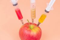 Chemical biology Syringes with different chemicals injections into a red apple on an orange background. GMO. Chemistry. Poison. Fruits. Place for an inscription. The close plan. Drugs. fruit,healthcare,nature