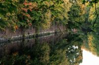 canal body Autumn trees reflect perfectly in the calm fort moat water of one of the 12 Königsberg forts in Kaliningrad, with stone embankment at the base. 