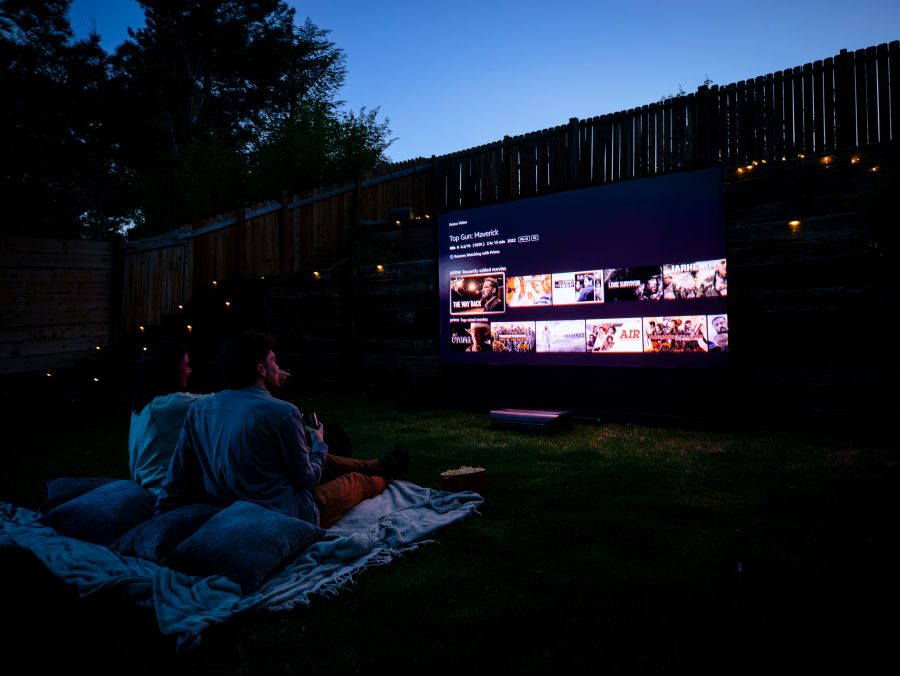 Outdoor cinema Two people sitting on a blanket, immersed in a movie experience enhanced by AWOL Vision 4K UST projector. 