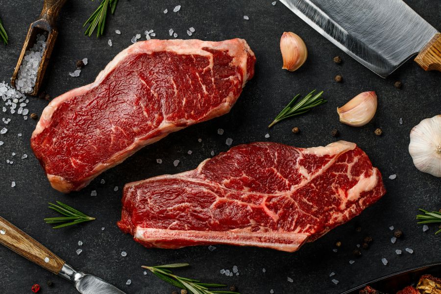 beef Raw striploin and bone-steak with knife, rosemary, salt and pepper top view 