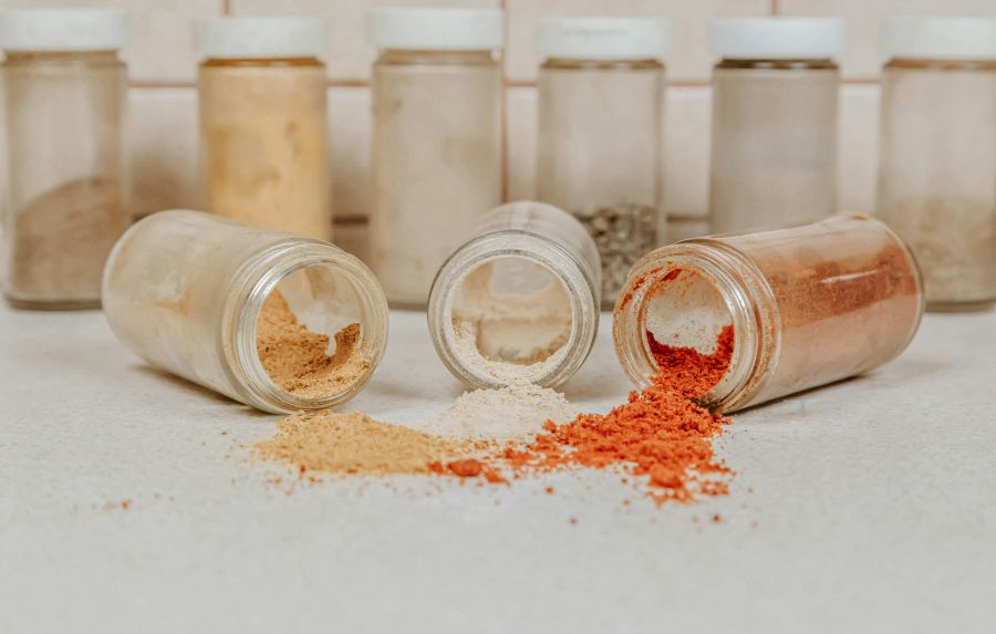 food additives Jars with different scattered assortment of spices, white pepper, chili flakes, lemongrass, coriander and cumin seeds in jars on kitchen. Advertising 