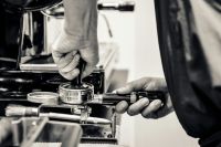 Frank Meunier A barista is tamping his coffee at a coffee bar and there is a blurred espresso machine in the background. coffee grind,coffee ground,frank leuderalbert
