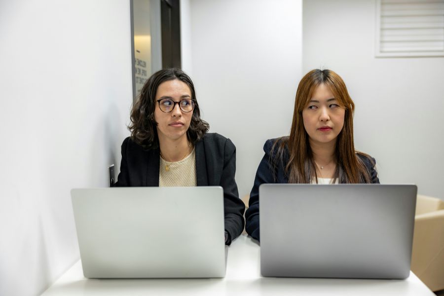 Conflict Tension Front view of two angry female employees using computers disputing at the workplace and looking sideways at each other with a grudge female,grey,office fights