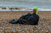 punk A punk rocker, dressed in leather, with green Mohican hair and wearing sunglasses, laying on the beach. uk,person,beach